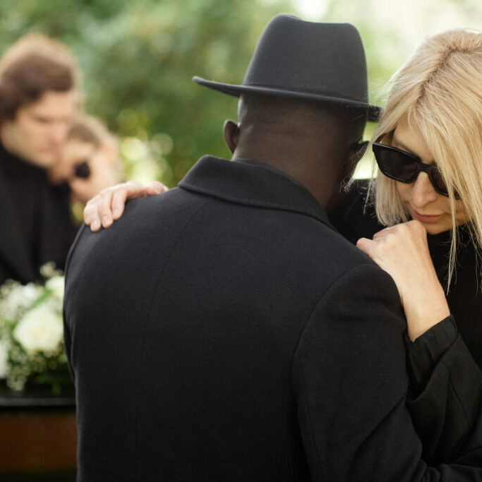 Two people embracing at outdoor funeral ceremony and wearing black